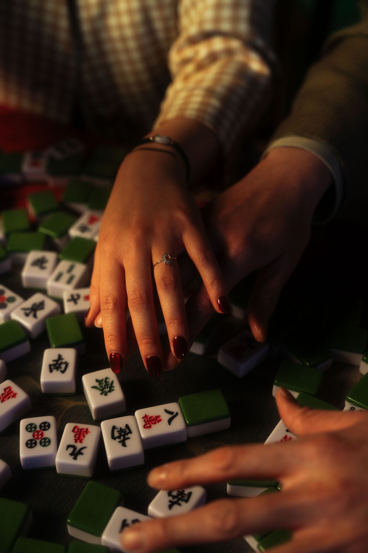 Julie's hand with the engagement ring resting over Teck Yan's, scattered across mahjong tiles