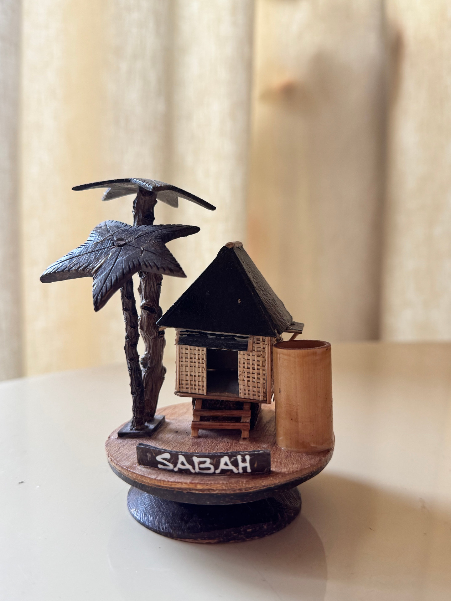 A small handcrafted wooden Sabah hut souvenir with a palm tree, from Kota Kinabalu